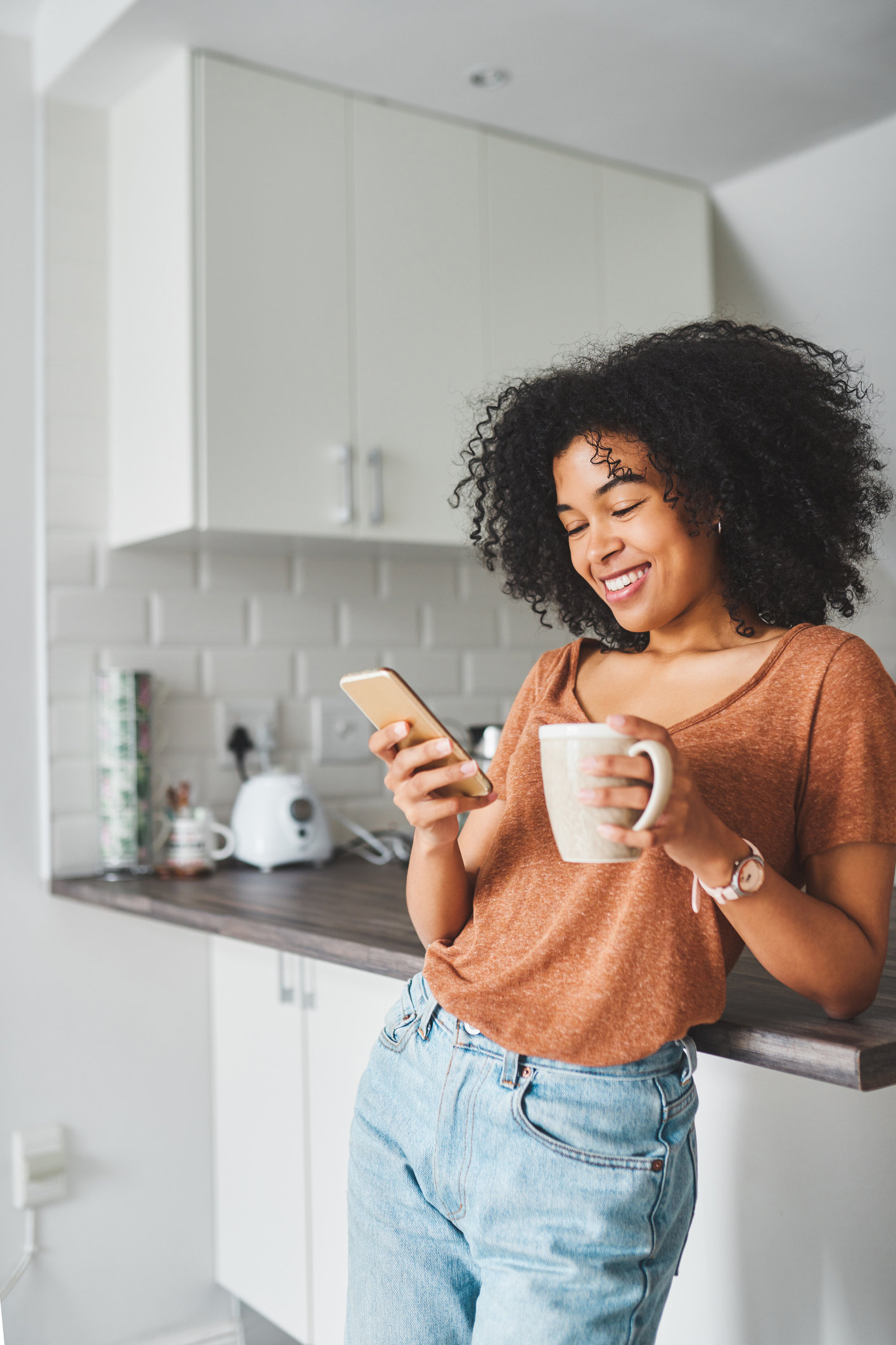 A woman in the kitchen looking at her smartphone and smiling.