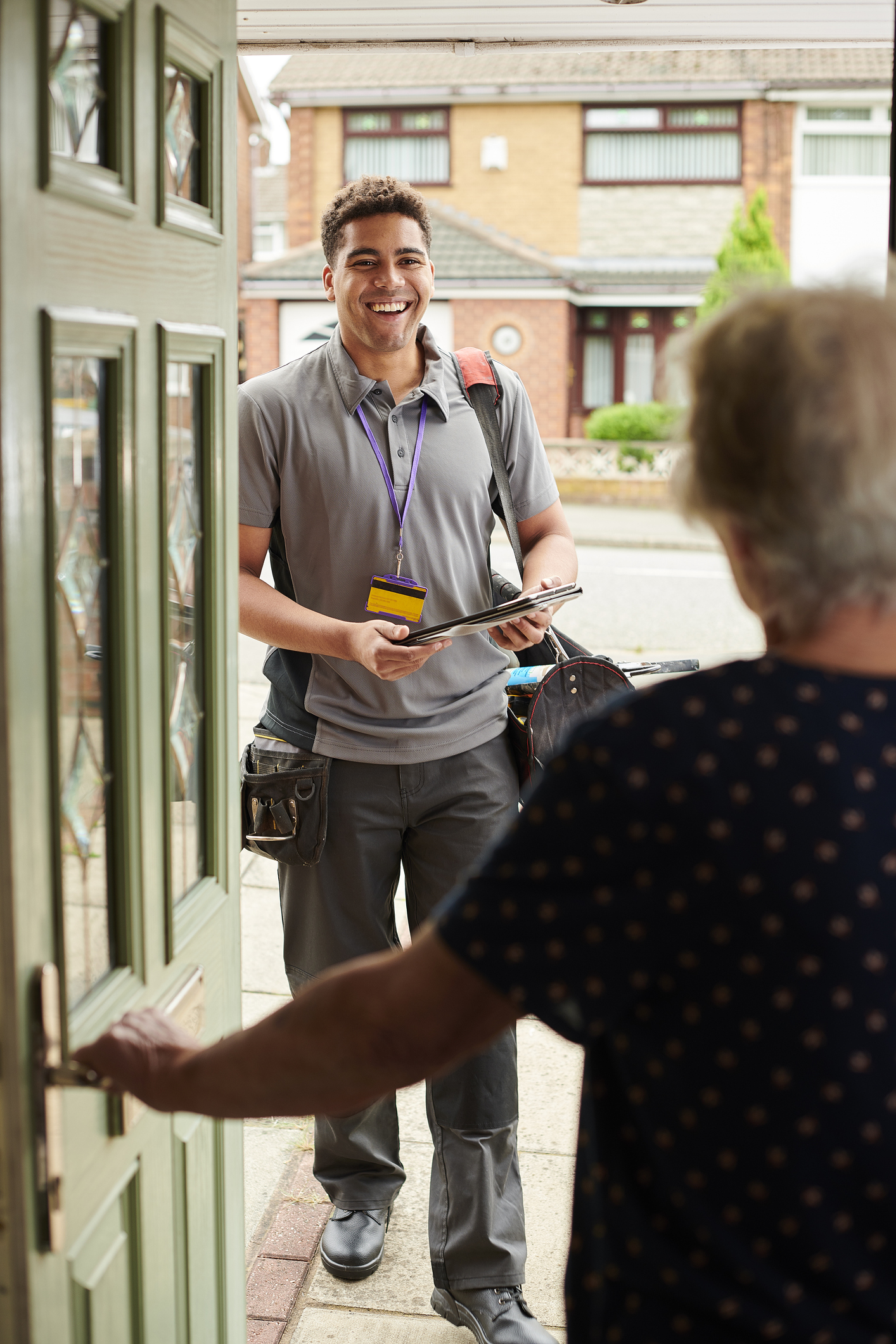 A contractor standing at the front door of a house, smiling while holding a clipboard, as an elderly woman opens the door.